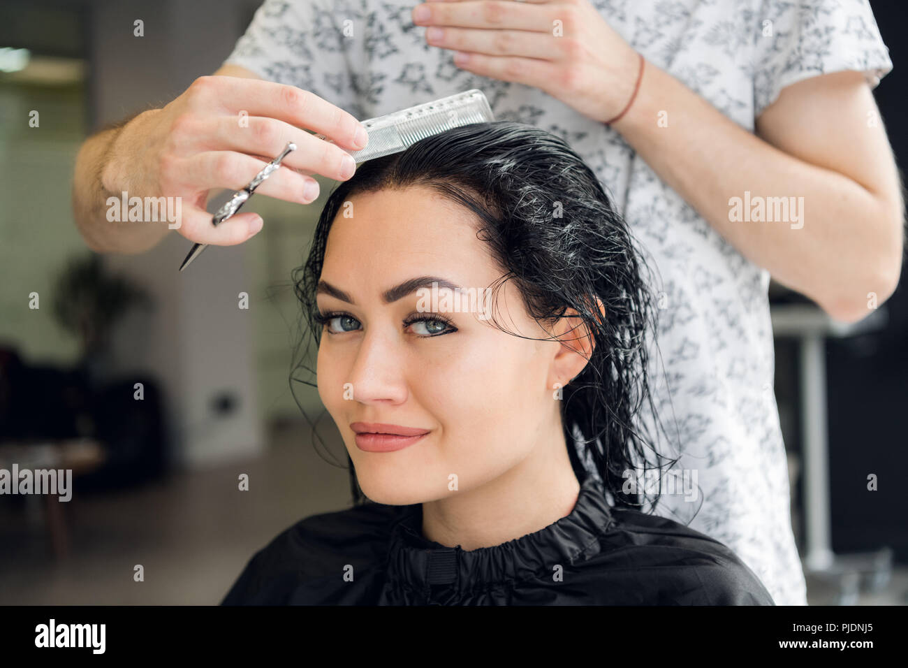 Hairdresser cutting woman's hair in salon, smiling, front view, close-up, portrait Stock Photo