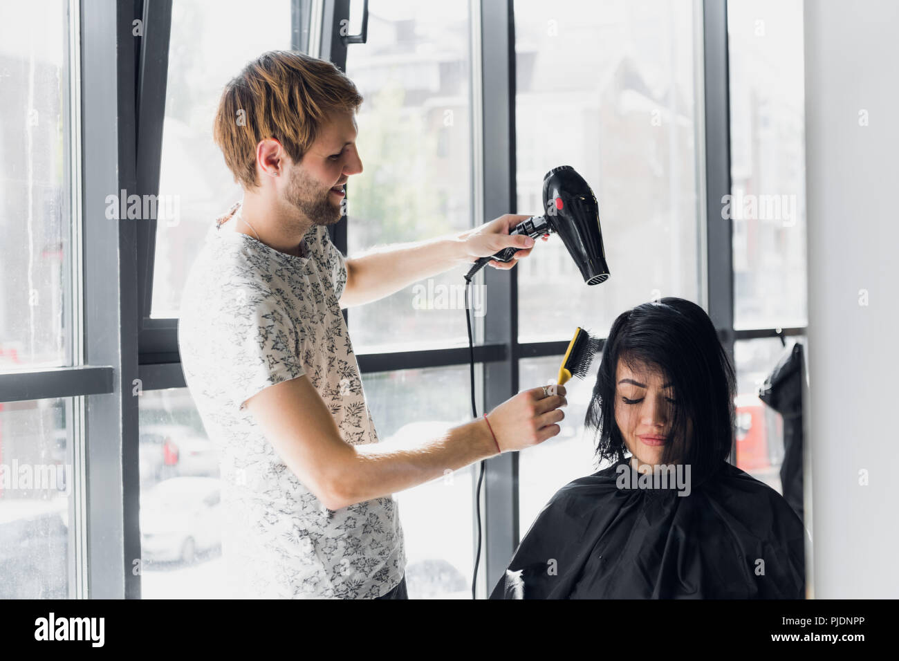Young woman getting her hair dressed in hair salon by a handsome