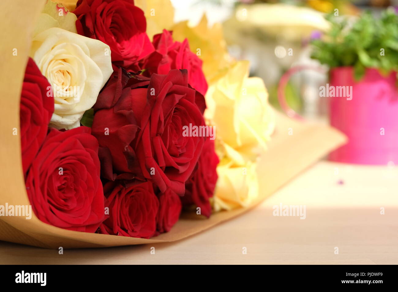 A bouquet of roses lies on a table as an anniversary gift. The strong red colors contrast with the white and brighter colors. Stock Photo