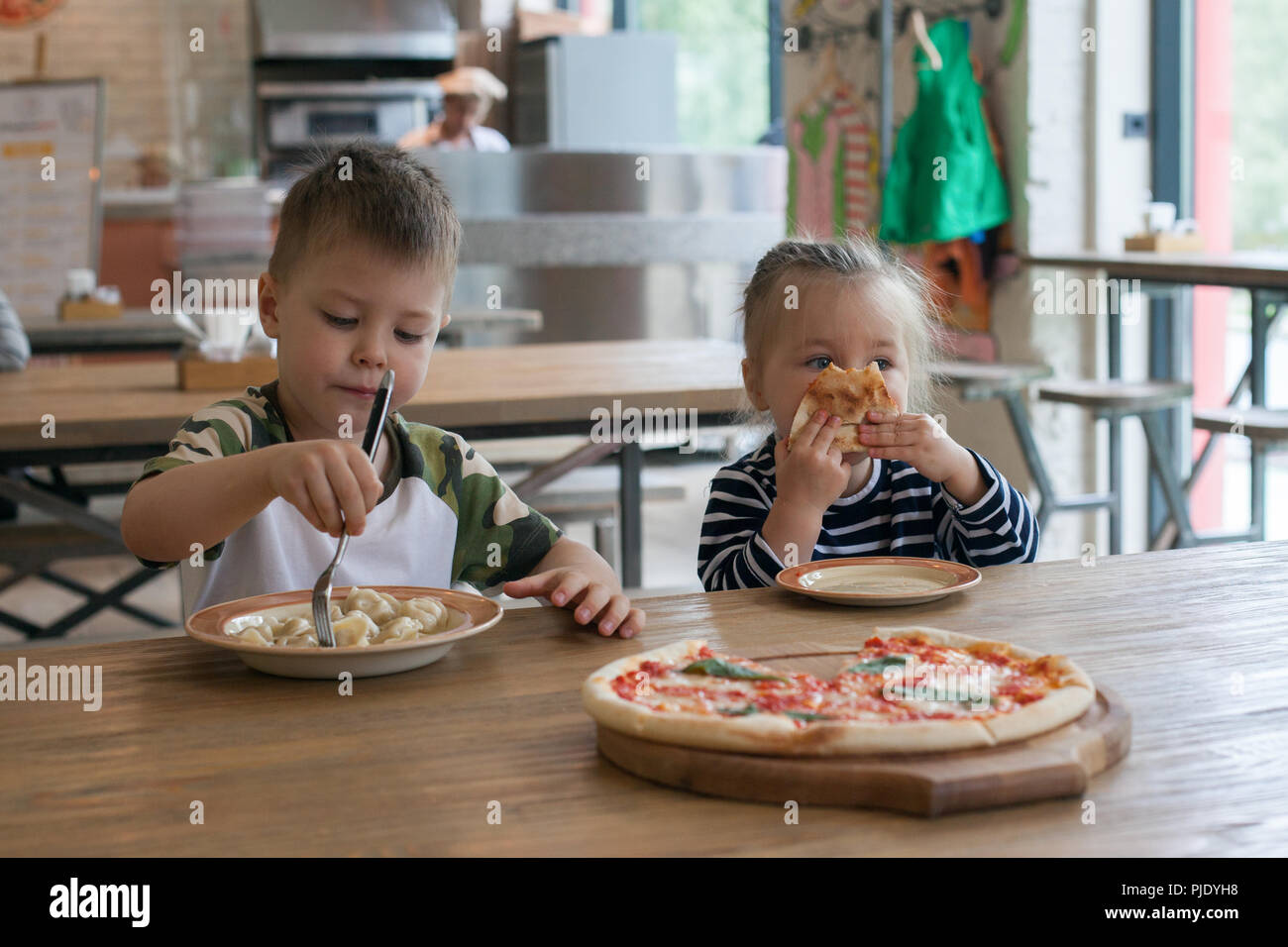 kids eat pizza and meat dumplings at cafe. children eating unhealthy food indoors. Siblings in the cafe, family holiday concept. Stock Photo