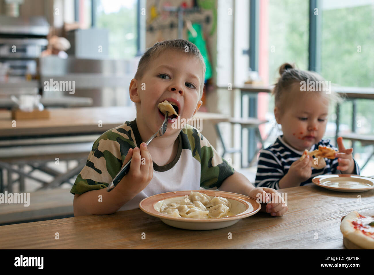 kids eat pizza and meat dumplings at cafe. children eating unhealthy food indoors. Siblings in the cafe, family holiday concept. Stock Photo