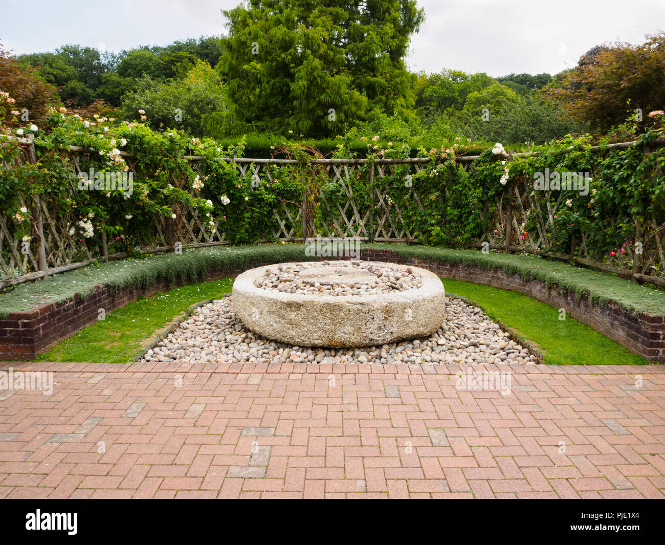 Rose smothered trellis and Chamomile seat surround an old millstone in the Sensory garden at Buckfast Abbey Stock Photo