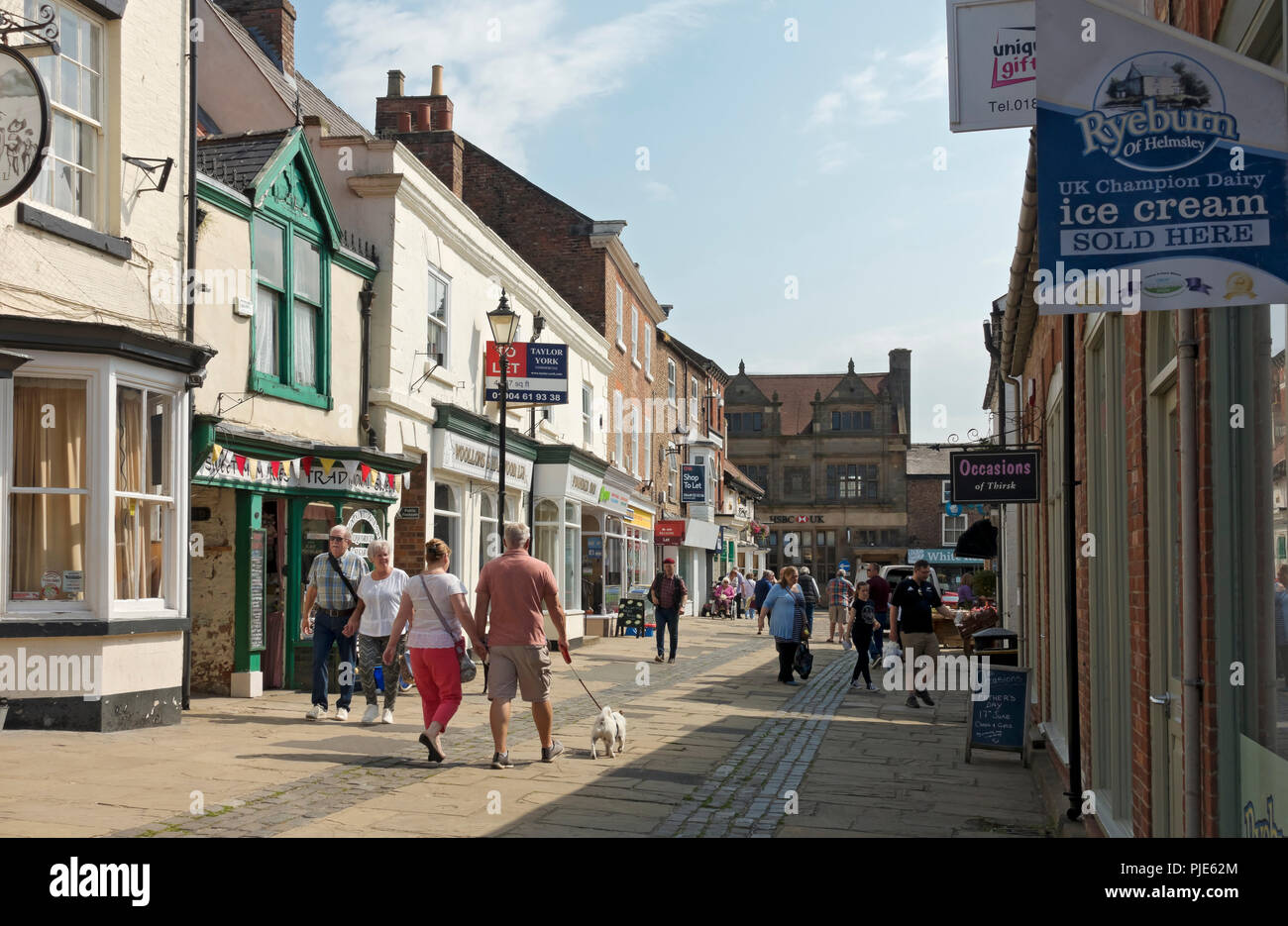Shoppers people walking in the town centre in summer Market Place Thirsk North Yorkshire England UK United Kingdom GB Great Britain Stock Photo