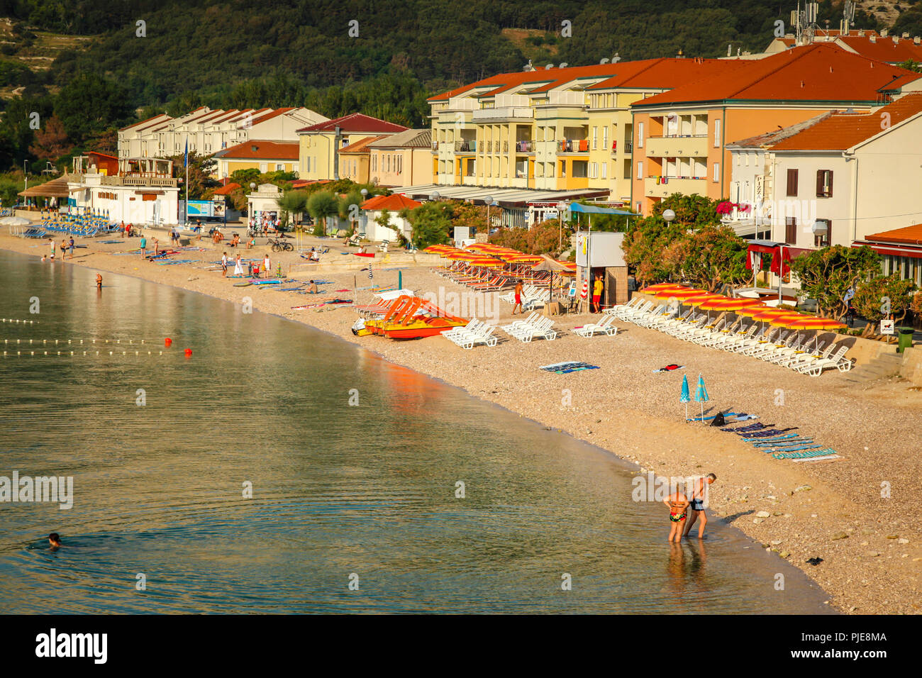 People enjoy the small beach at the hotel lined seaside resort village of Baska on the Croatian island of Krk in the Adriatic Sea Stock Photo