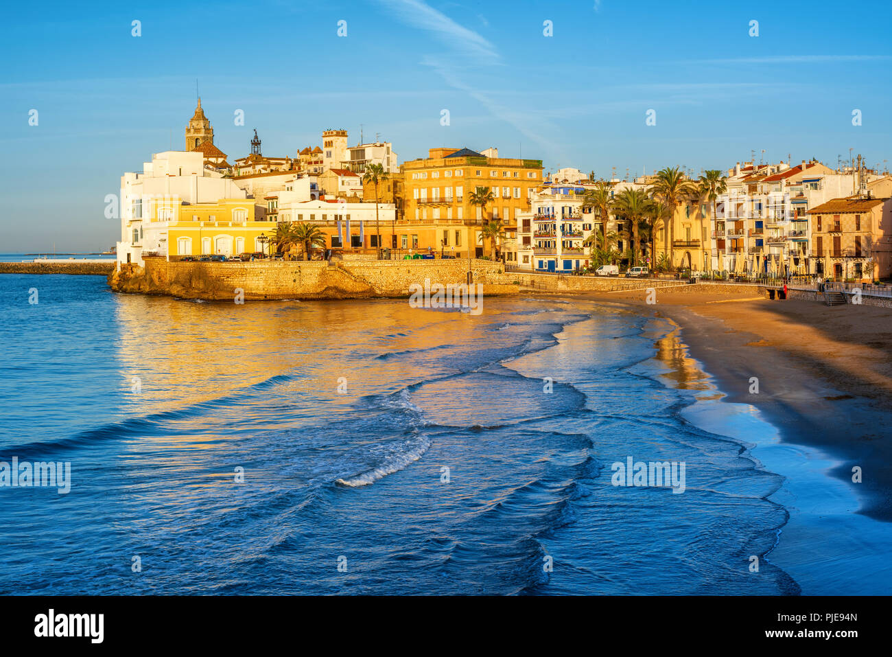 Fine sand beach and historical Old Town in mediterranean resort Sitges near Barcelona, Costa Dorada, Catalonia, Spain, in the early morning light Stock Photo