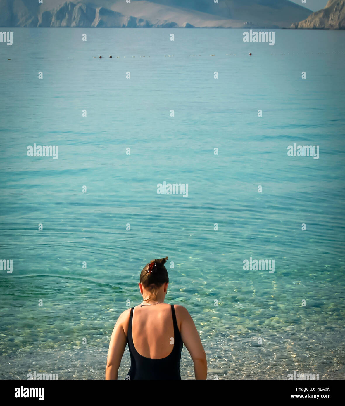 Back of woman in bathing suit as she paddles in the blue Adriatic Sea on the Croatian island of Krk in the resort town of Baska Stock Photo
