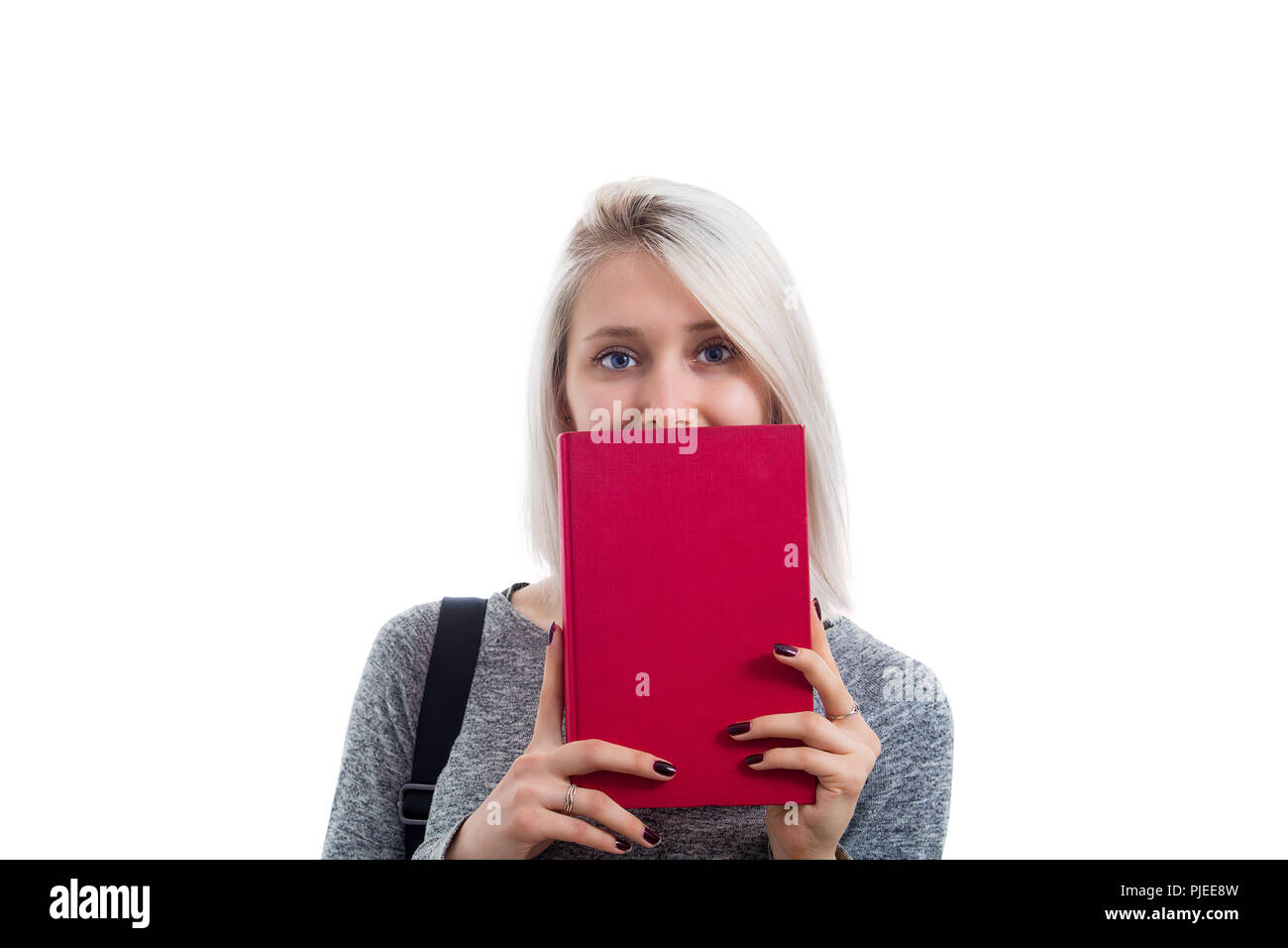 Shy woman student cover her mouth using a closed red book. Hide face expression, change identity isolated over white background. Stock Photo