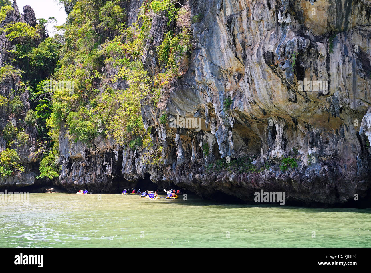 Tourists explore with the canoe eroded limestone rocks in the bay of Phang Nga, Thailand, Touristen erkunden mit dem Kanu erodierte Kalksteinfelsen in Stock Photo