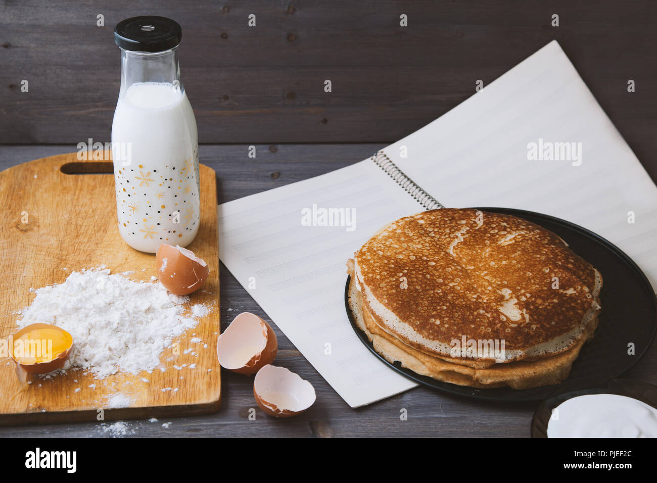 fresh, hot pancakes in a frying pan, eggs, milk, flour on a wooden