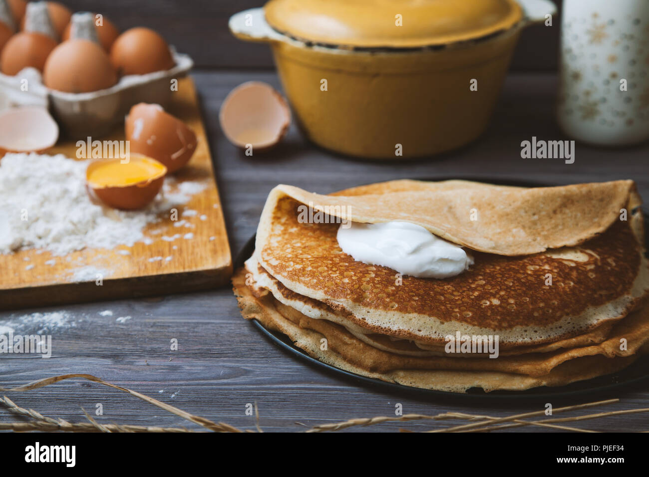 fresh, hot pancakes in a frying pan, eggs, milk, flour on a wooden