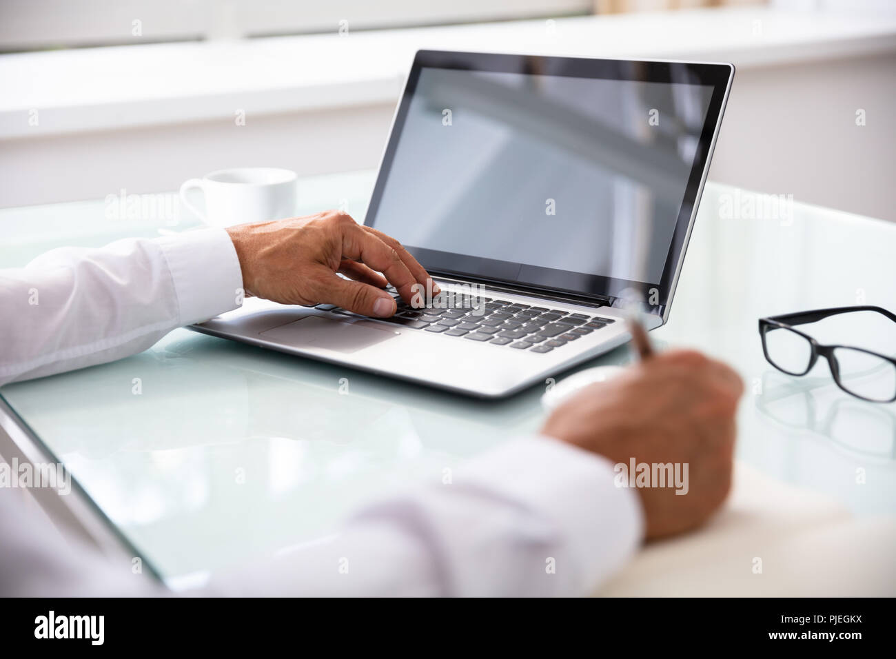 Businessman's Hand Using Laptop While Writing Schedule In Diary Stock Photo
