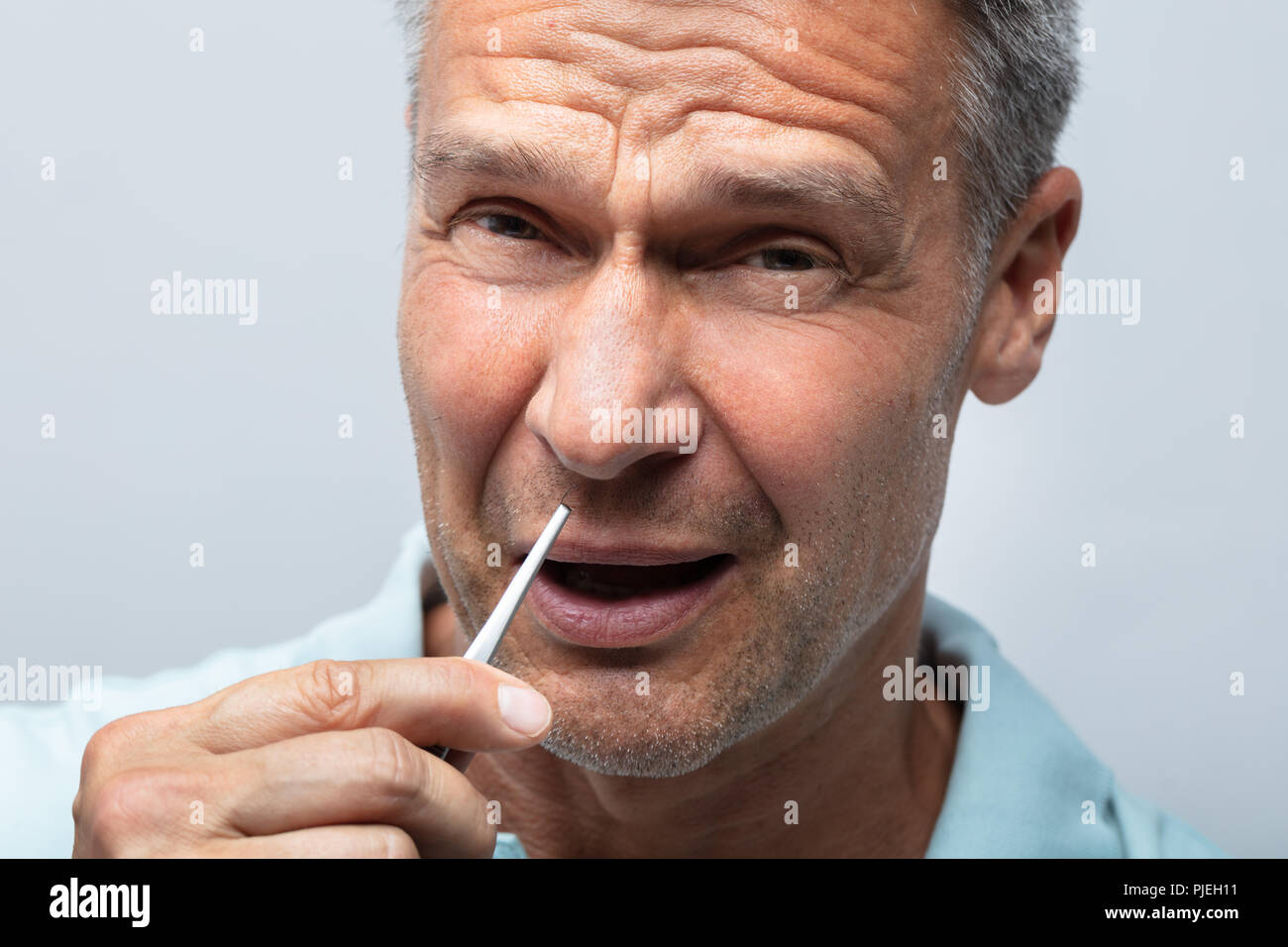 Close Up Of A Mature Man In Pain Removing Nose Hair With Tweezers
