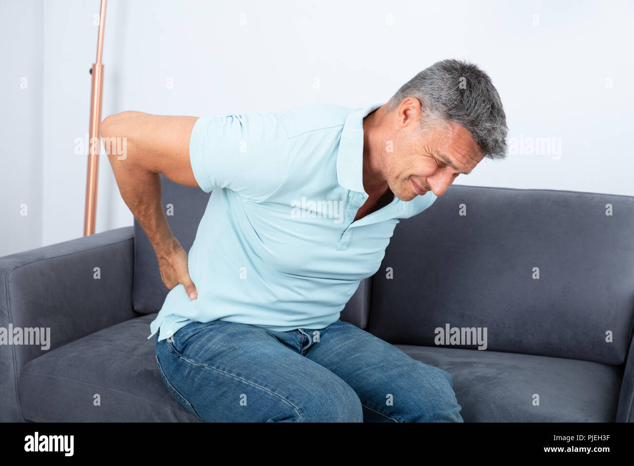 Mature Man Sitting On Sofa Suffering From Back Pain Stock Photo - Alamy