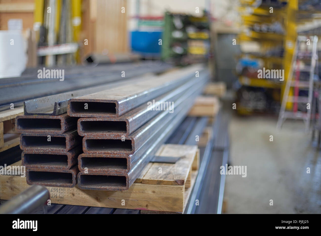 Structural steel tubes stacked on a skid, with material storage racks and fabrication plant in background Stock Photo