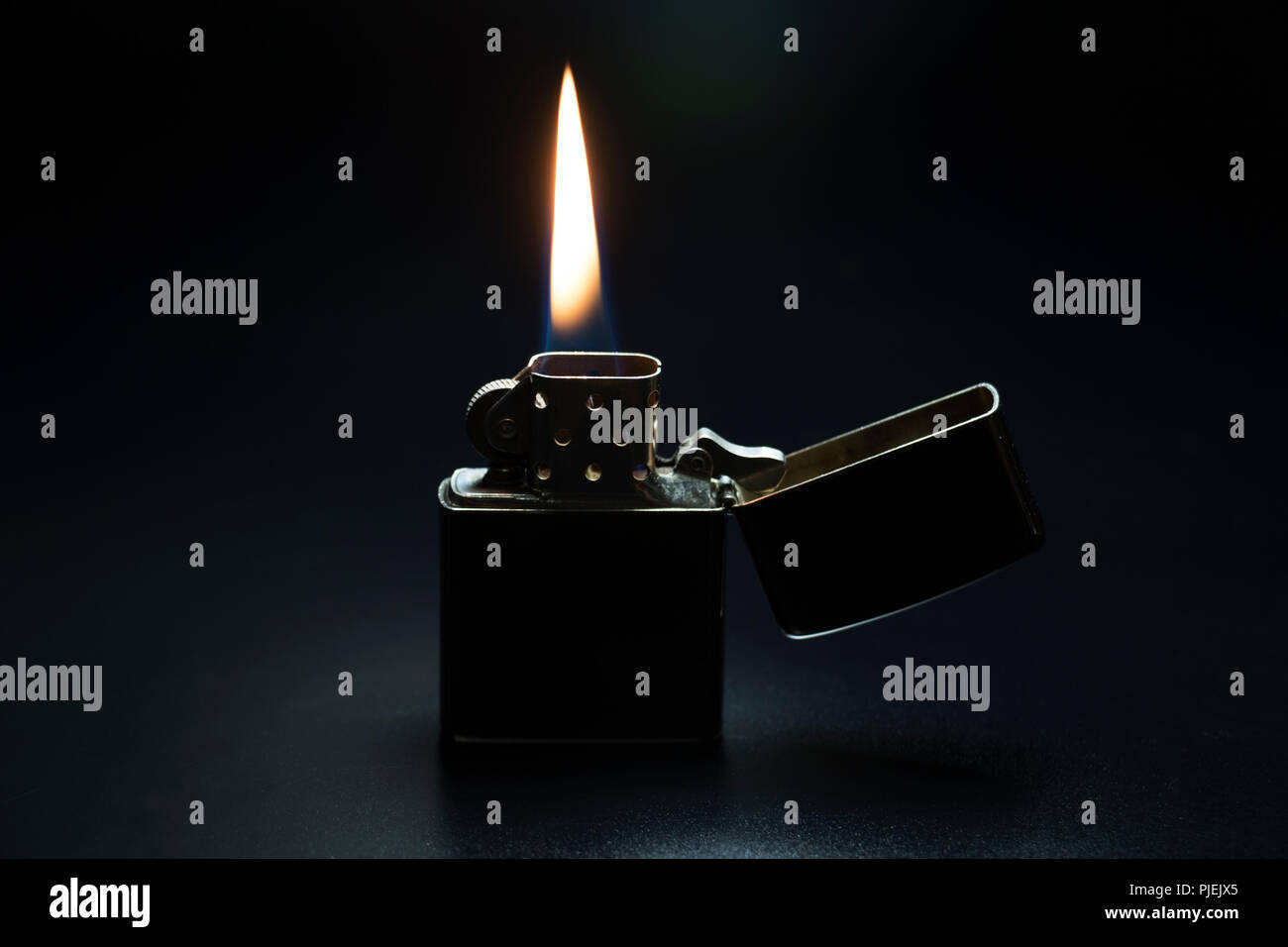 Lighter burning in darkness. Metallic lighter with red hot flame isolated on black background. Stock Photo