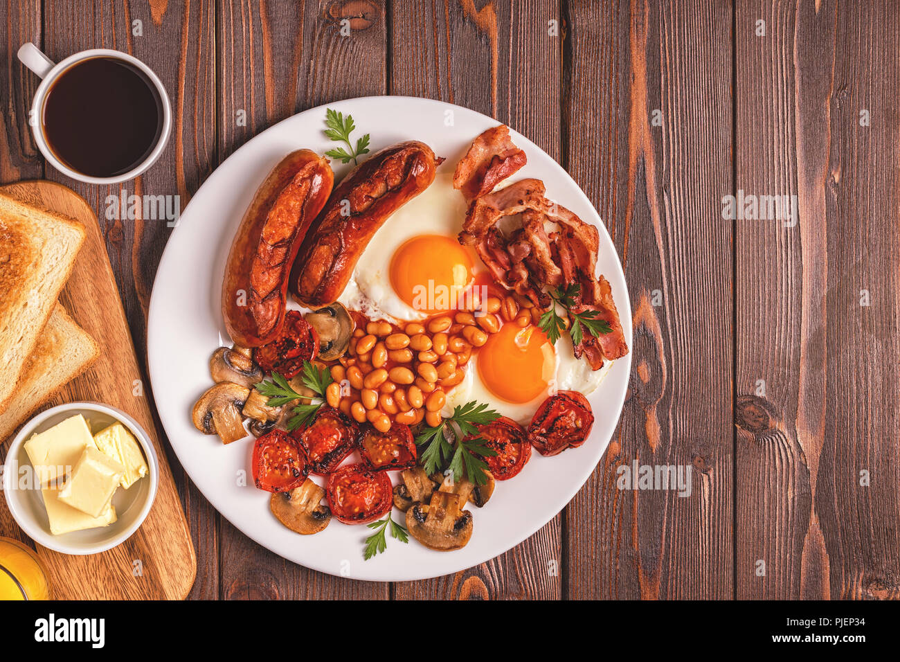 Traditional full English breakfast with fried eggs, sausages, beans, mushrooms, grilled tomatoes and bacon on wooden background. Top view Stock Photo