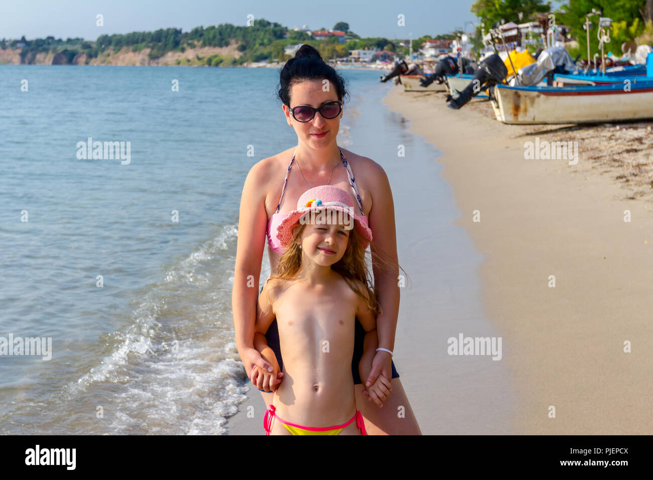 Happy child girl in summer hat is with her mom relaxing at the beach on sunny. Stock Photo