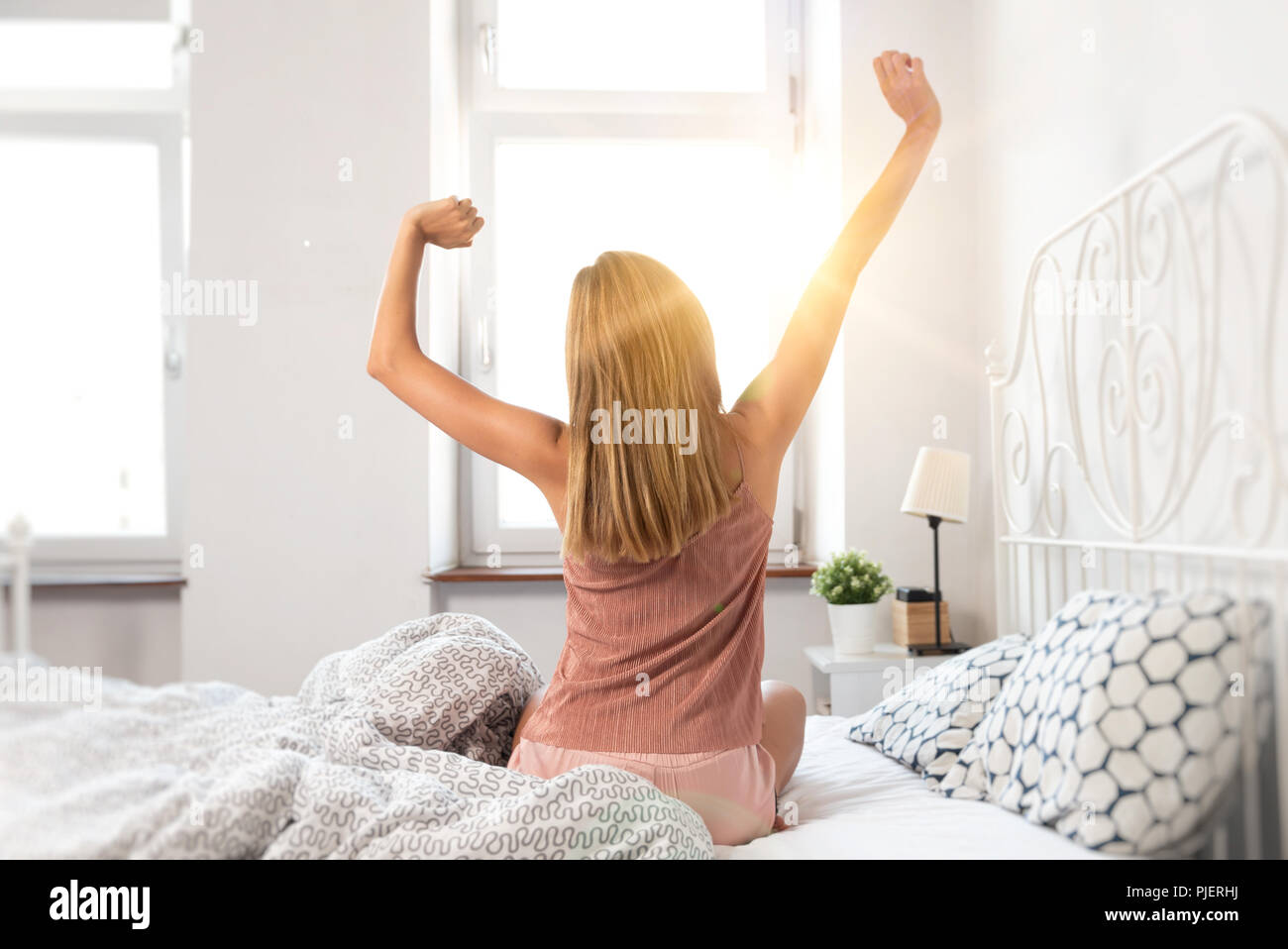 Back view of woman stretching in bed. Wake up at sunrise Stock Photo