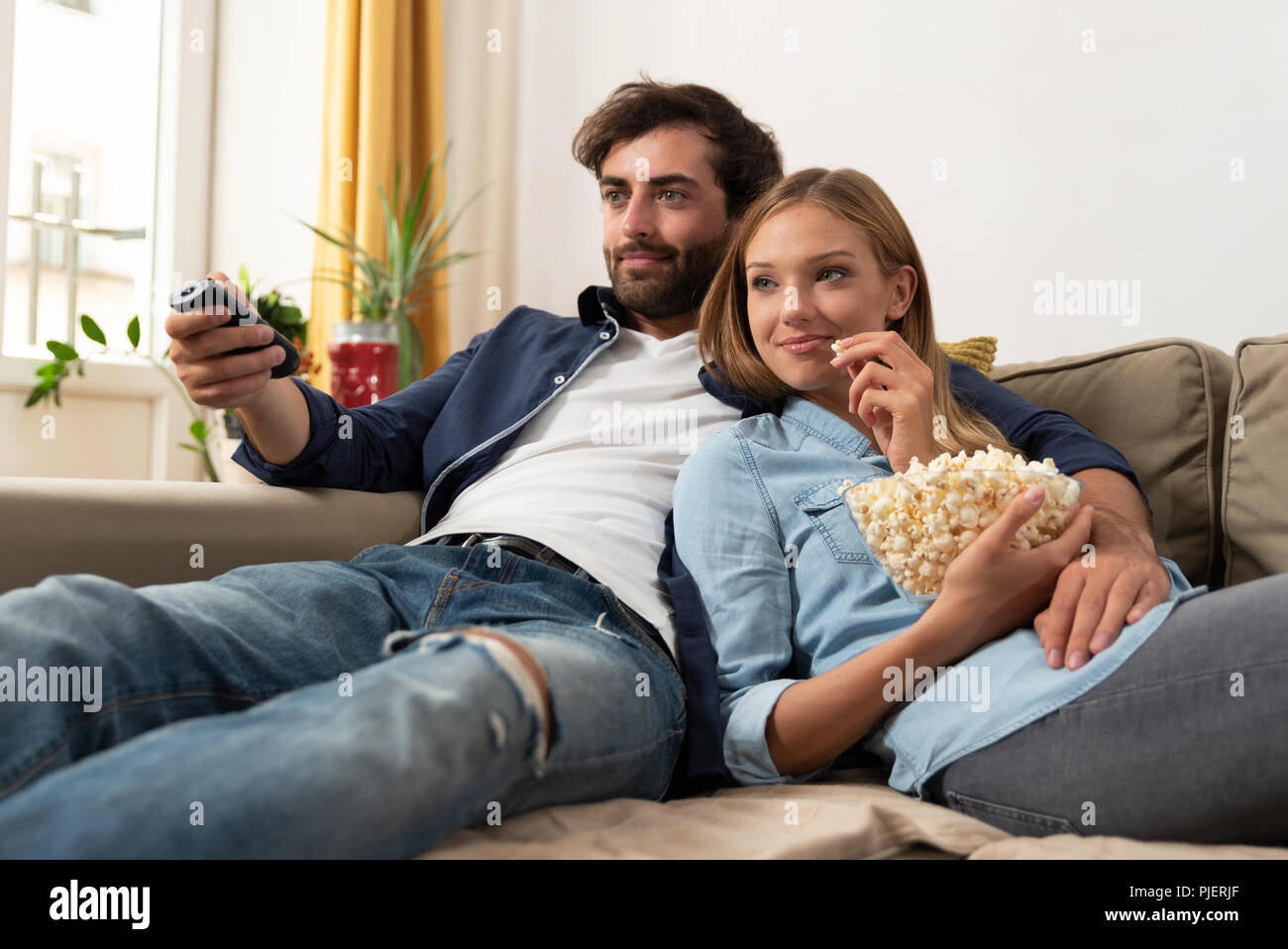 Couple watching TV, eating popcorn on a sofa at home Stock Photo - Alamy
