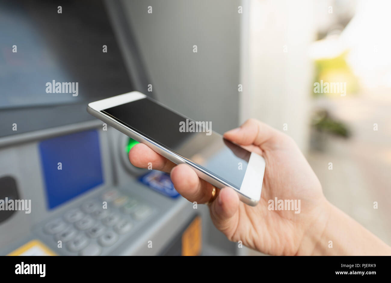 Withdraw money from an ATM without using a credit card. Person holding a phone and using mobile banking. Stock Photo