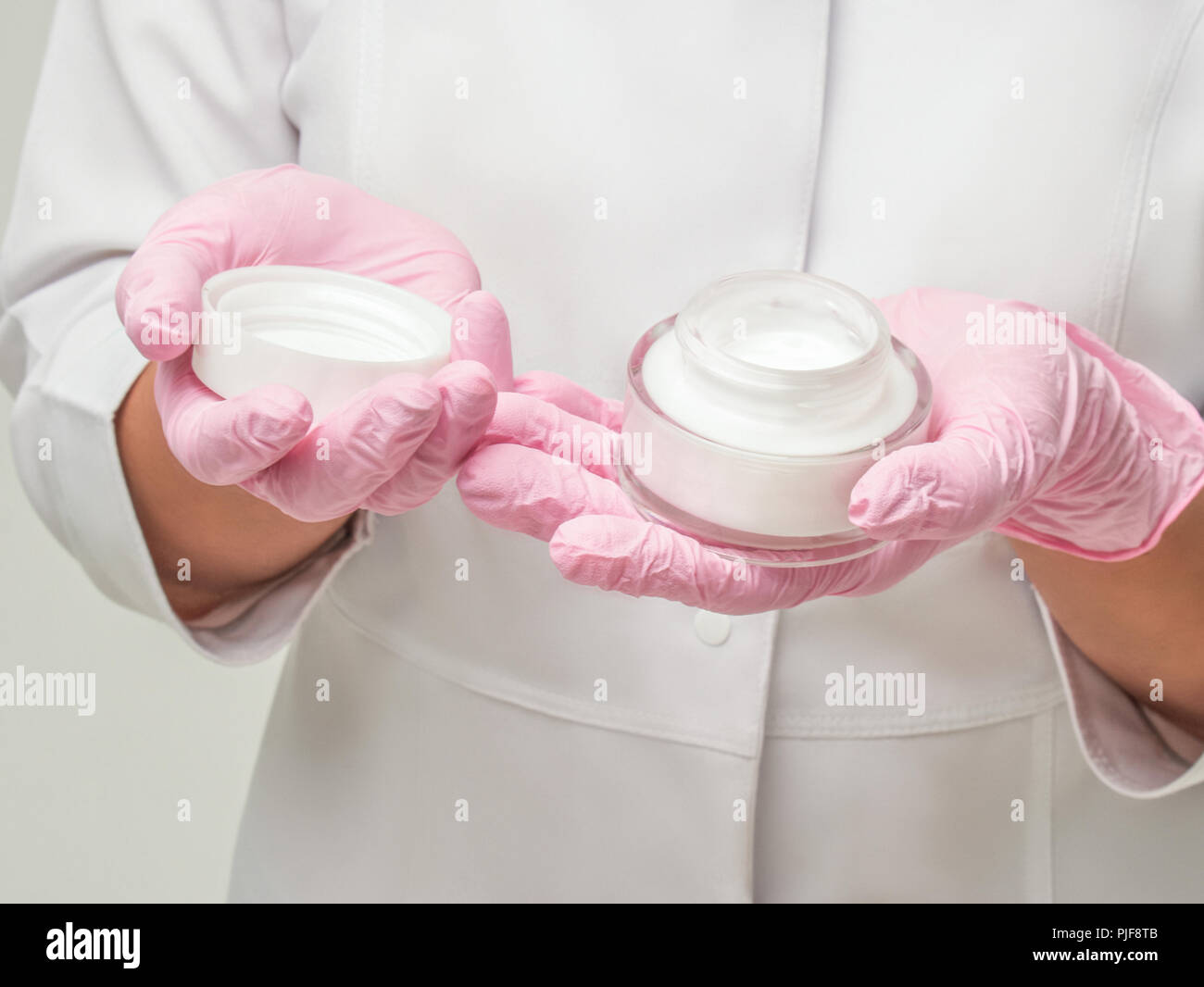 Doctor opening a jar of cream. Doctor Cosmetologist works in a clinic. Cosmetic means and skin cream. Hand in pink Gloves with Cream Jar. Stock Photo