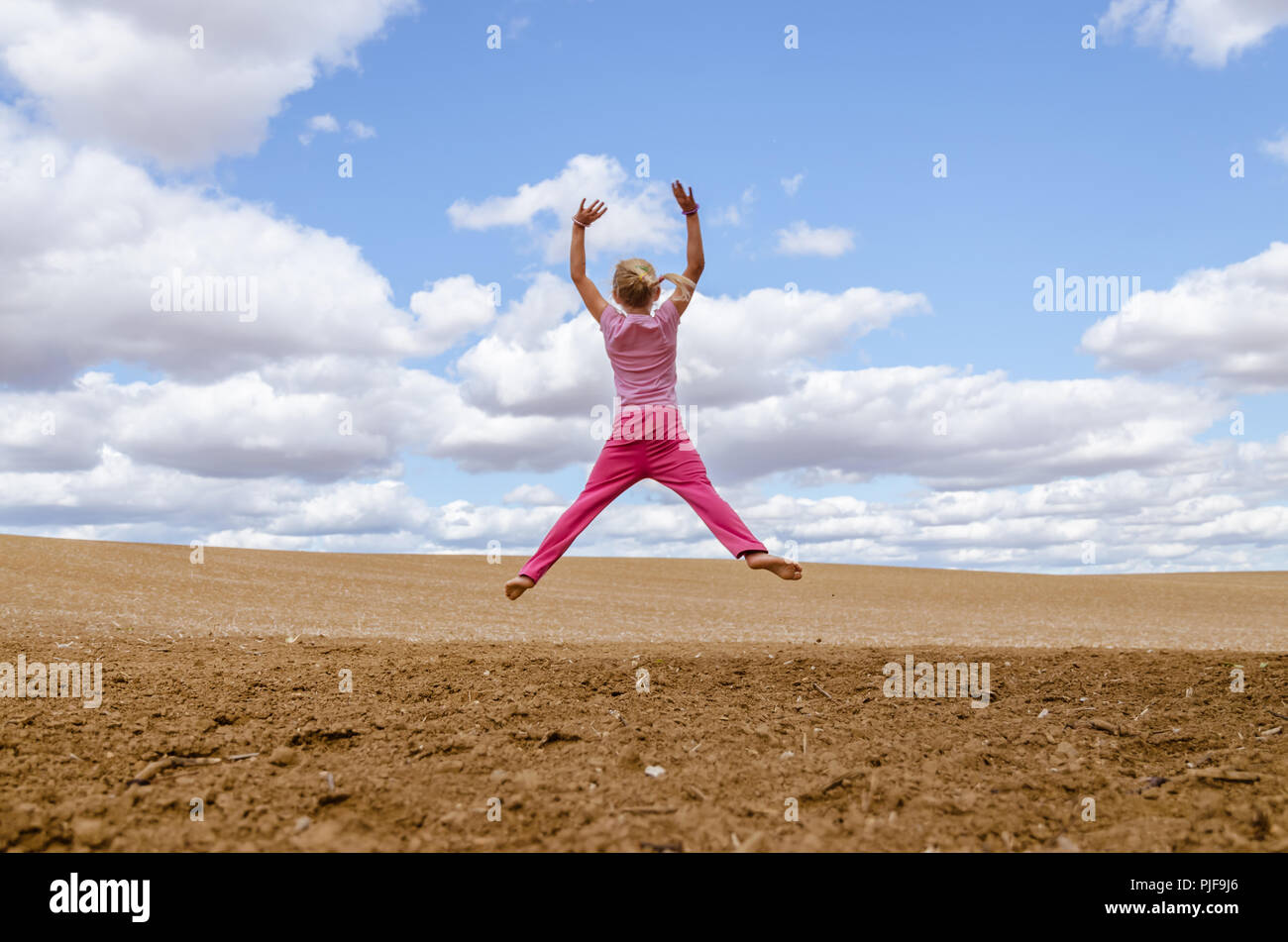 little child jumping alone in country in scenic countryside with beautiful clouds and blue sky Stock Photo