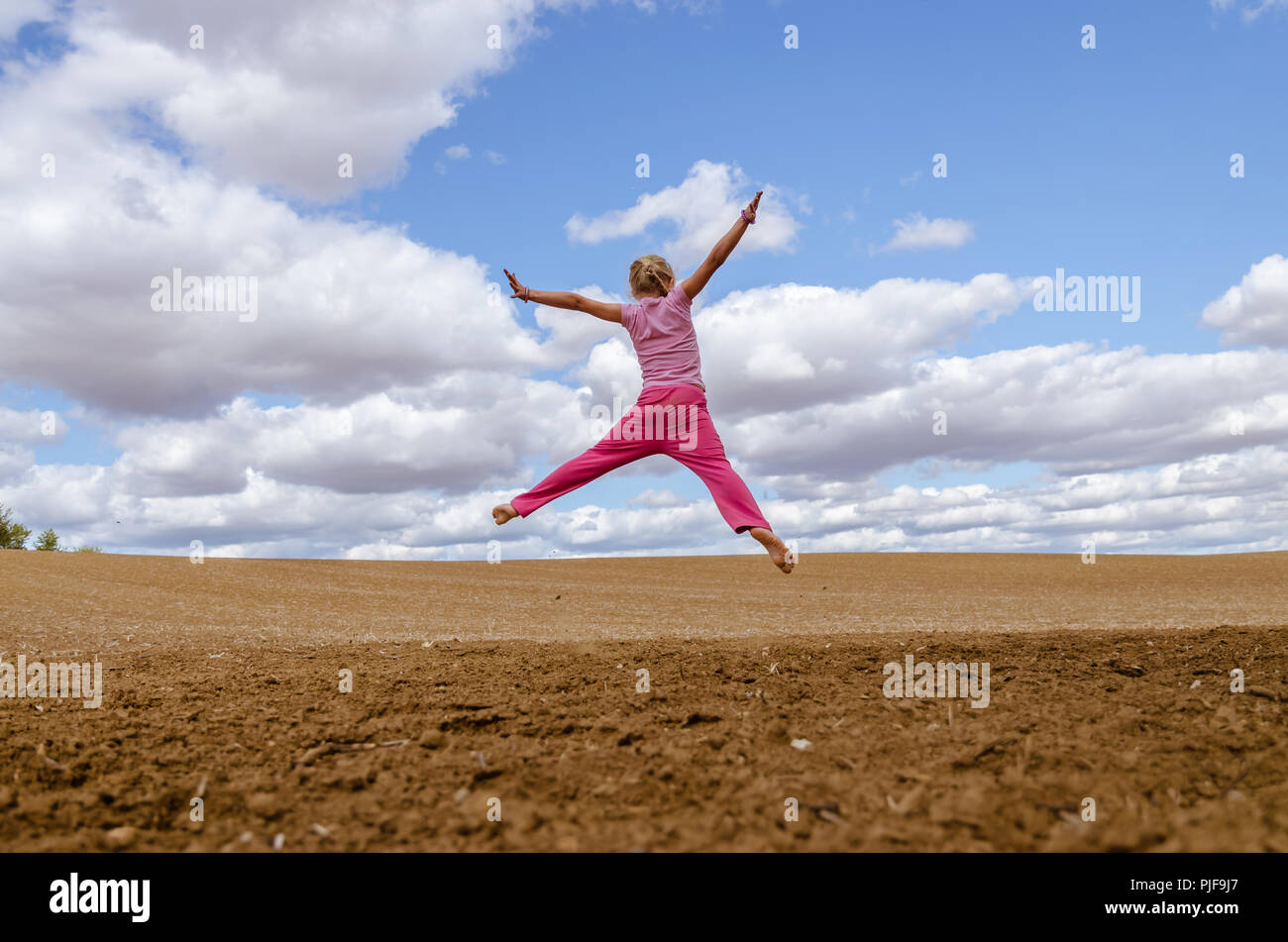 little child jumping alone in country in scenic countryside with beautiful clouds and blue sky Stock Photo