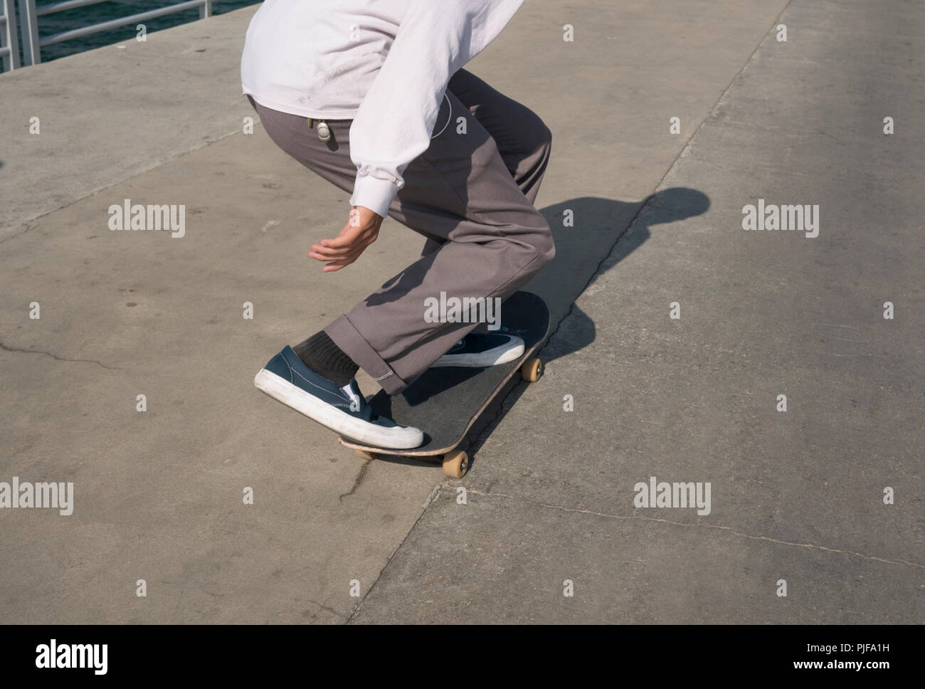 Young male skates low on a pier Stock Photo