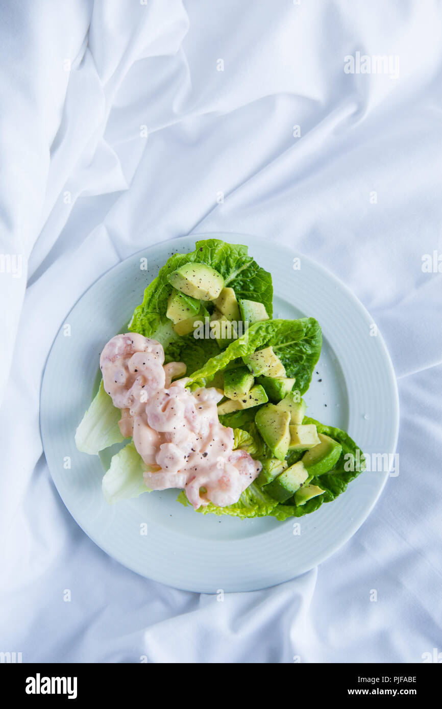 Classic prawn cocktail with pink marie rose sauce served with chopped  avocado nestled in sweet cos lettuce cups on a white plate on crumpled  white bed Stock Photo - Alamy