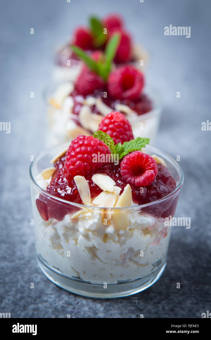 Risalamande is a cold Danish rice pudding served here in three small glass containers in a row on a grey background, as a dessert with cherry jam, fla Stock Photo