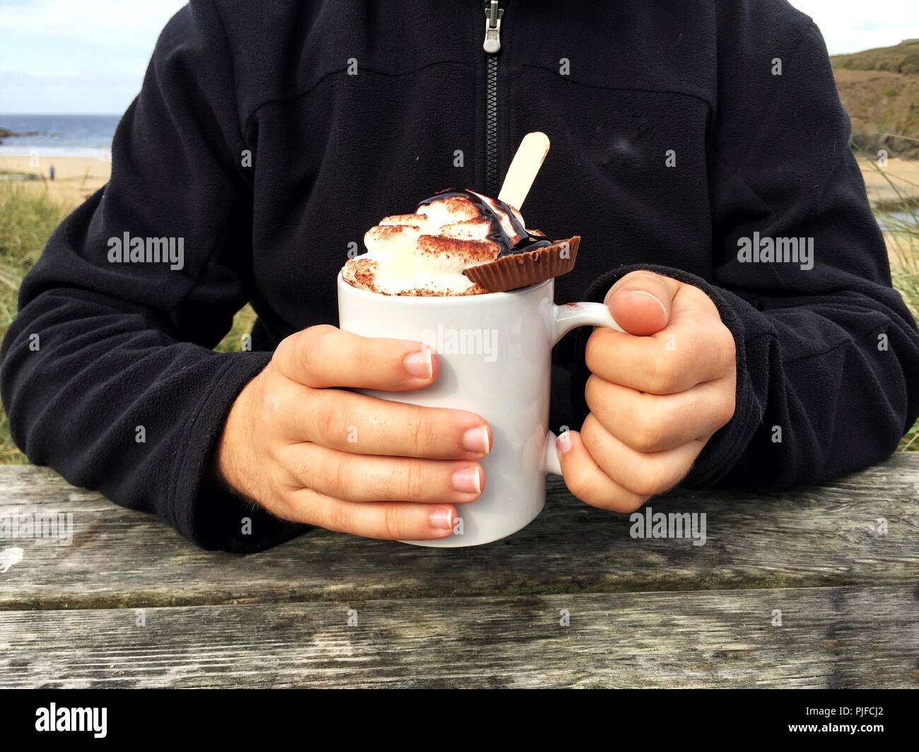 A midsection of a male holding a cup of indulgent hot chocolate with whipped cream and cookies on top Stock Photo