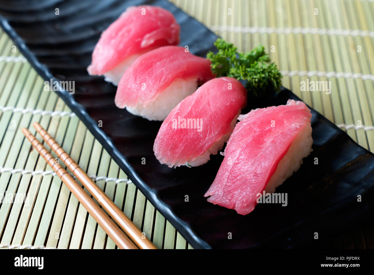 Tuna sushi on black plate along with Japanese sauce and green leaf decoration, Japanese food, close up at sushi . Stock Photo