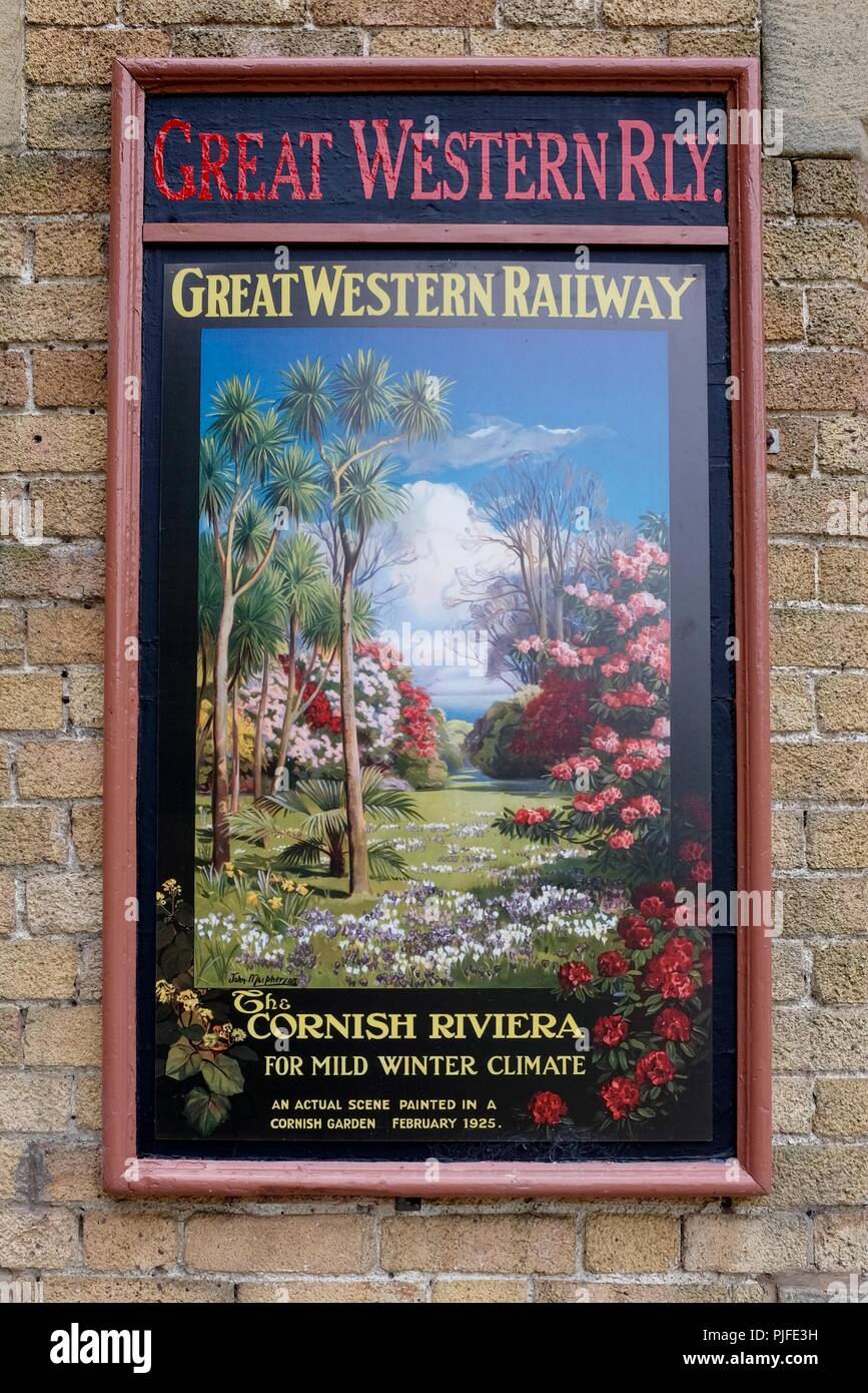 Close up of colourful vintage Great Western Railway poster for the Cornish Riviera with lush vegetation promoting mild winter weather on brick wall Stock Photo