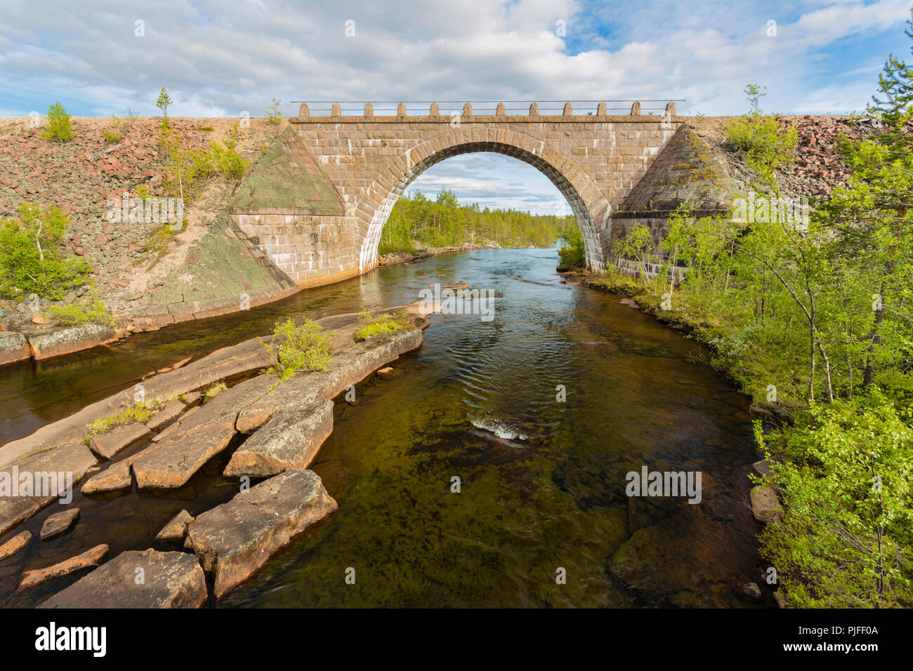 Old railroad bridge made of bricks with a portal, running water from river under it and forest in background, Jokkmokk county, Swedish Lapland, Sweden Stock Photo