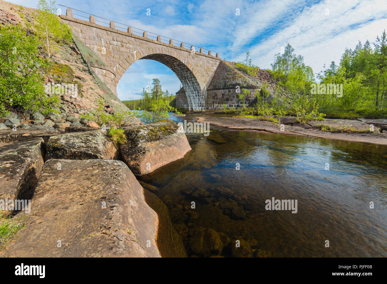 Old railroad bridge made of bricks with a portal, running water from river under it and forest in background, Jokkmokk county, Swedish Lapland, Sweden Stock Photo