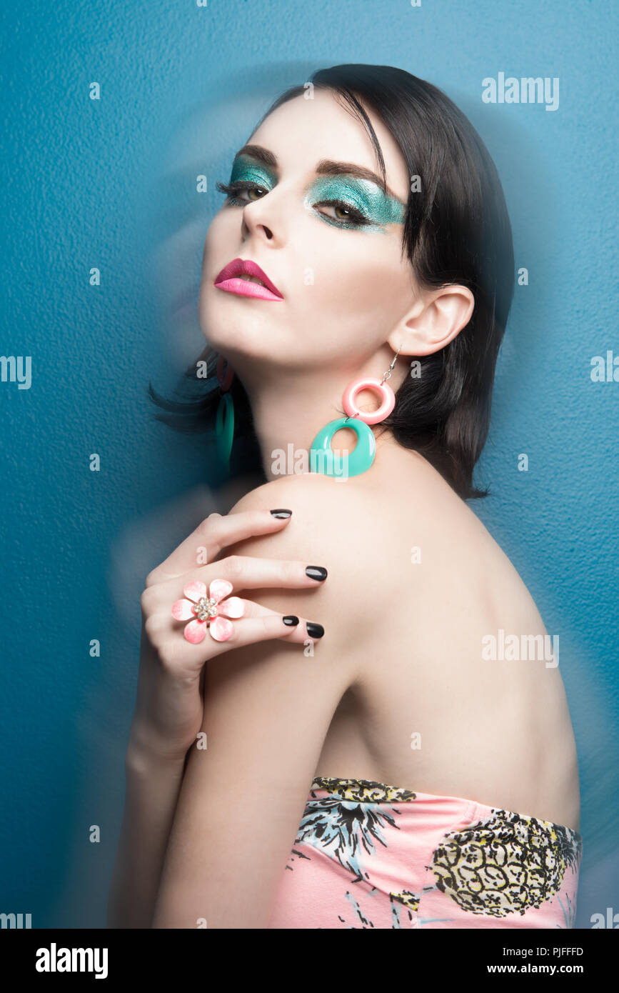 A pretty black hair female fashion model with blue eye make-up wearing 60s style mod earrings, a fashion accessory portrait concept Stock Photo