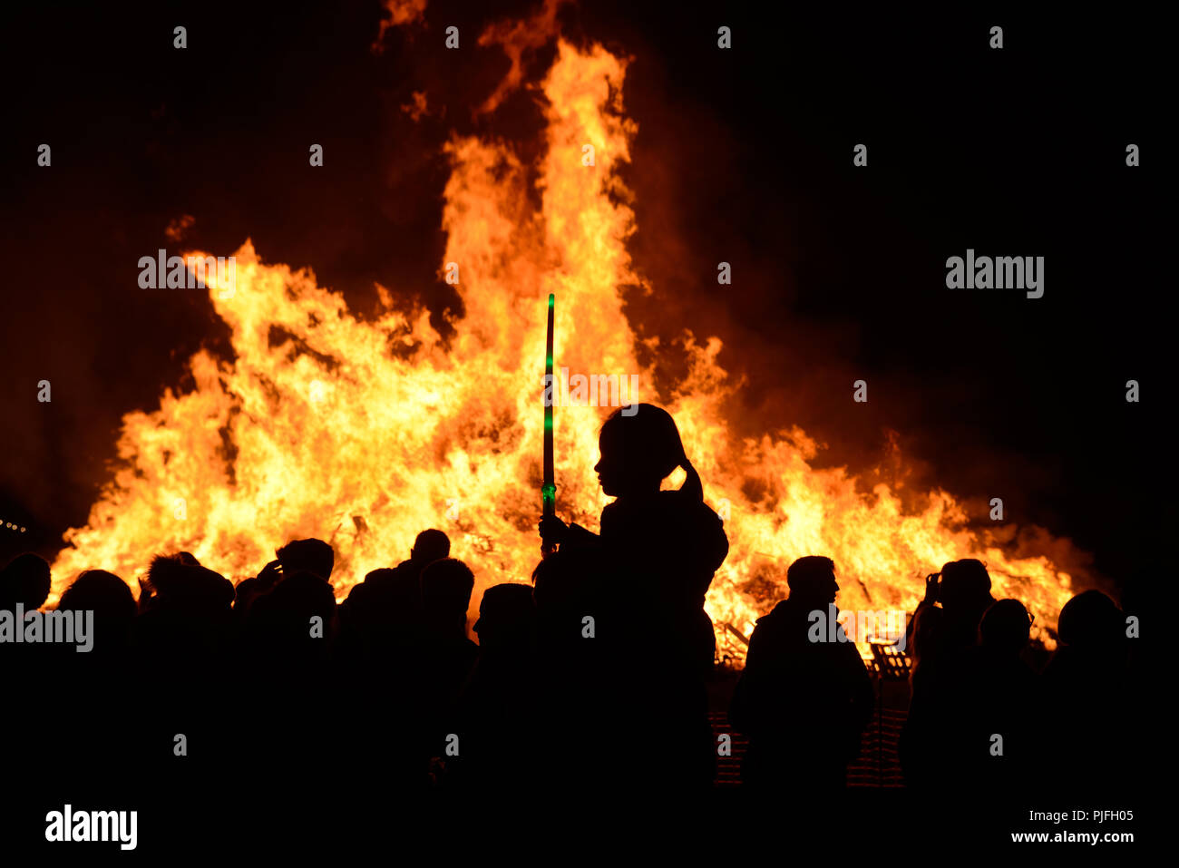 A child and people are silhouetted against the flames of a large bonfire on the 5th of November, Guy Fawkes Night, Bonfire Night. Stock Photo