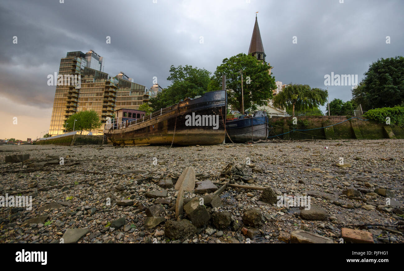 Houseboats are beached on the side of the River Thames at low tide beside Battersea Church in west London. Stock Photo