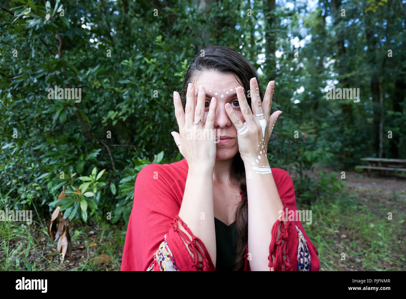 Young brunette hippie woman covering her face with her hand with white tribal make up Stock Photo