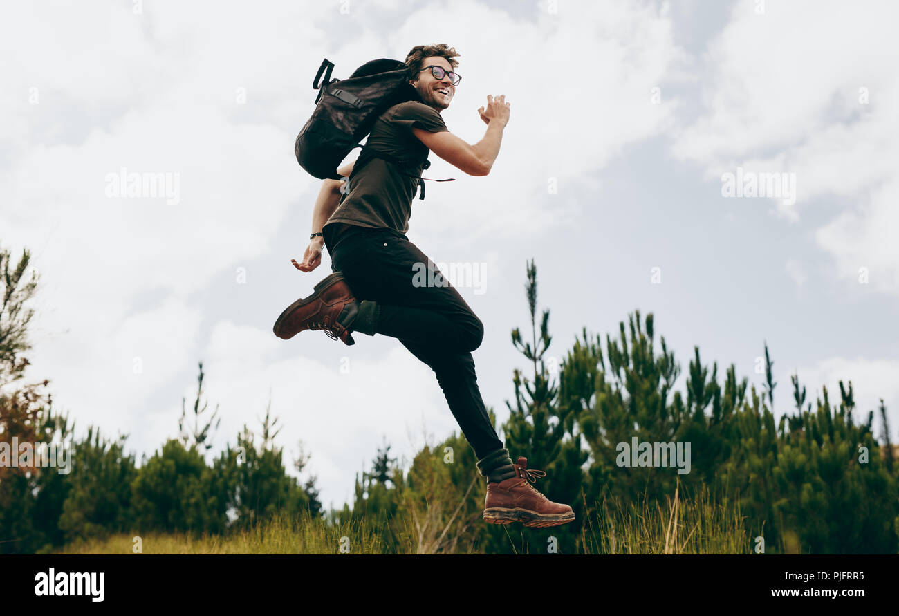 Man wearing a backpack jumping in air while trekking in the woods. Excited man on a holiday hiking in a countryside location. Stock Photo