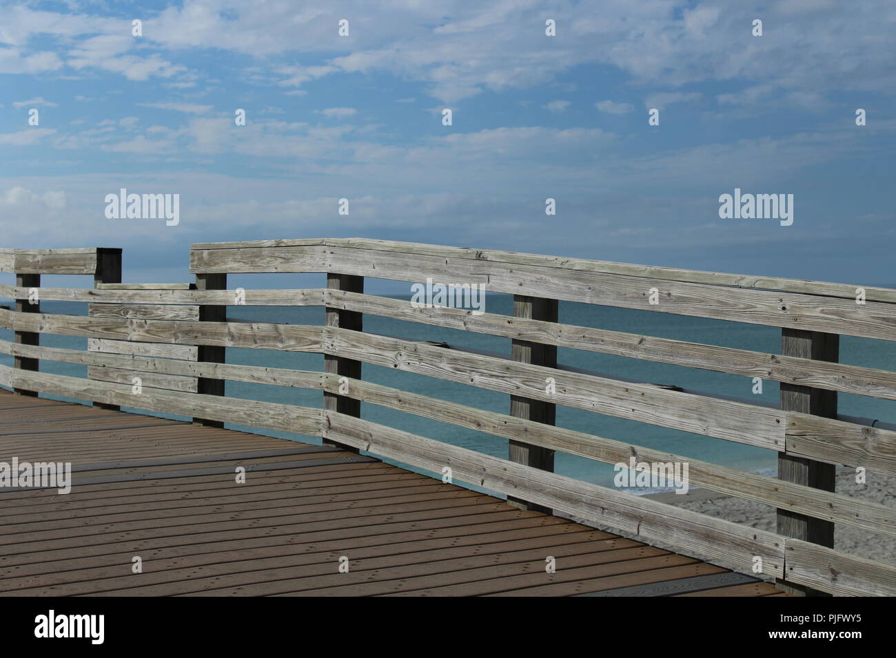 wooden fence on a pier by the ocean on a sunny day Stock Photo