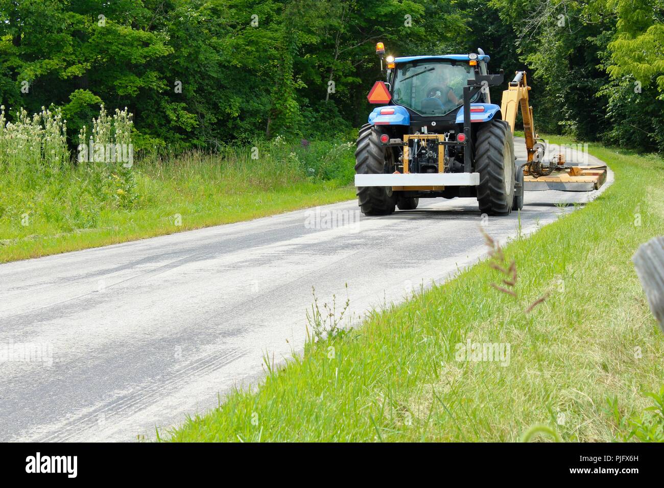 tractor cutting grass along side of a rural road Stock Photo