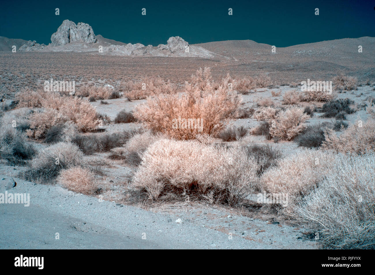 The Mojave Desert in color infrared with large rock formations, desert brush and fields under a blue sky. Stock Photo