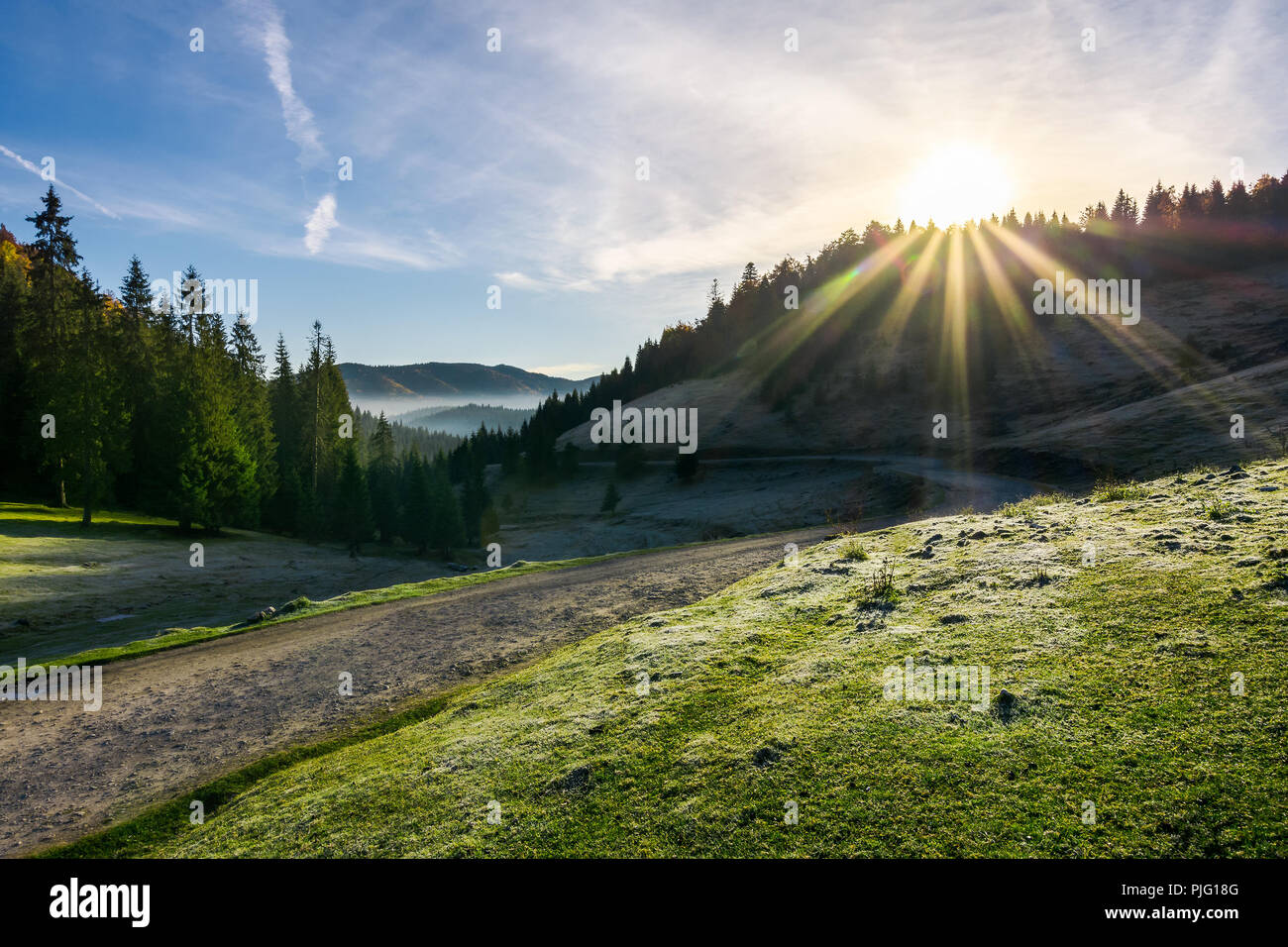 beautiful foggy landscape in autumn. winding road leads to distant valley full of fog. sun rise above the mountain. hoar on the grassy meadow Stock Photo