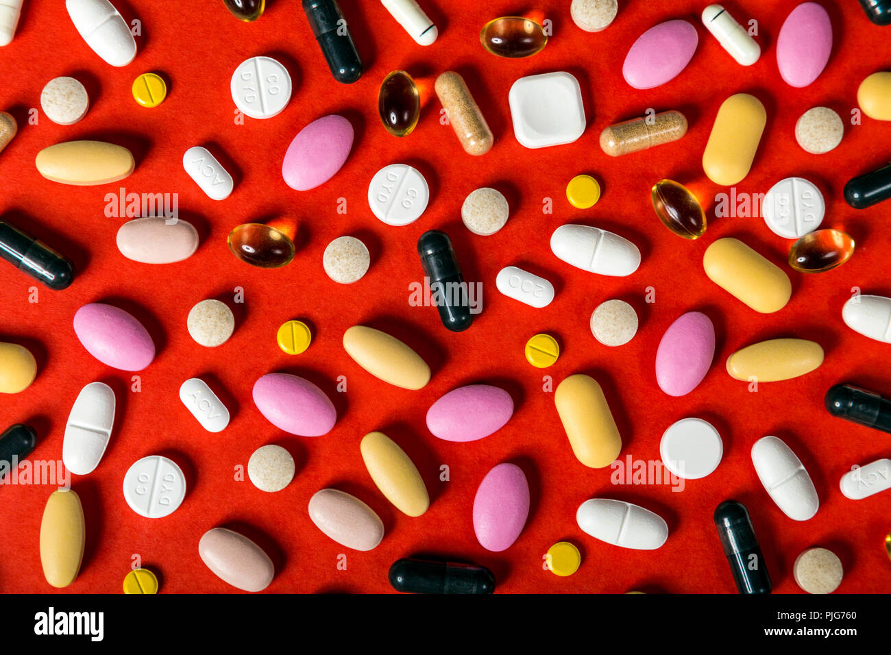 Scattered pills, capsules and tablets against red background, supplements, medication, healthcare Stock Photo