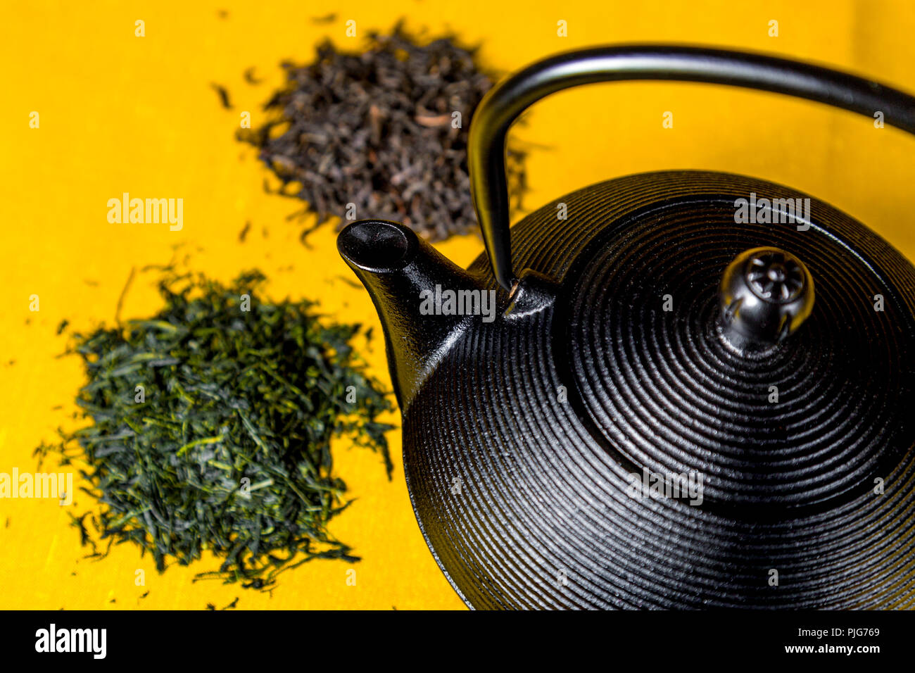 Cast Iron teapot (tetsubin) with loose leaf black and green tea piles against yellow background Stock Photo