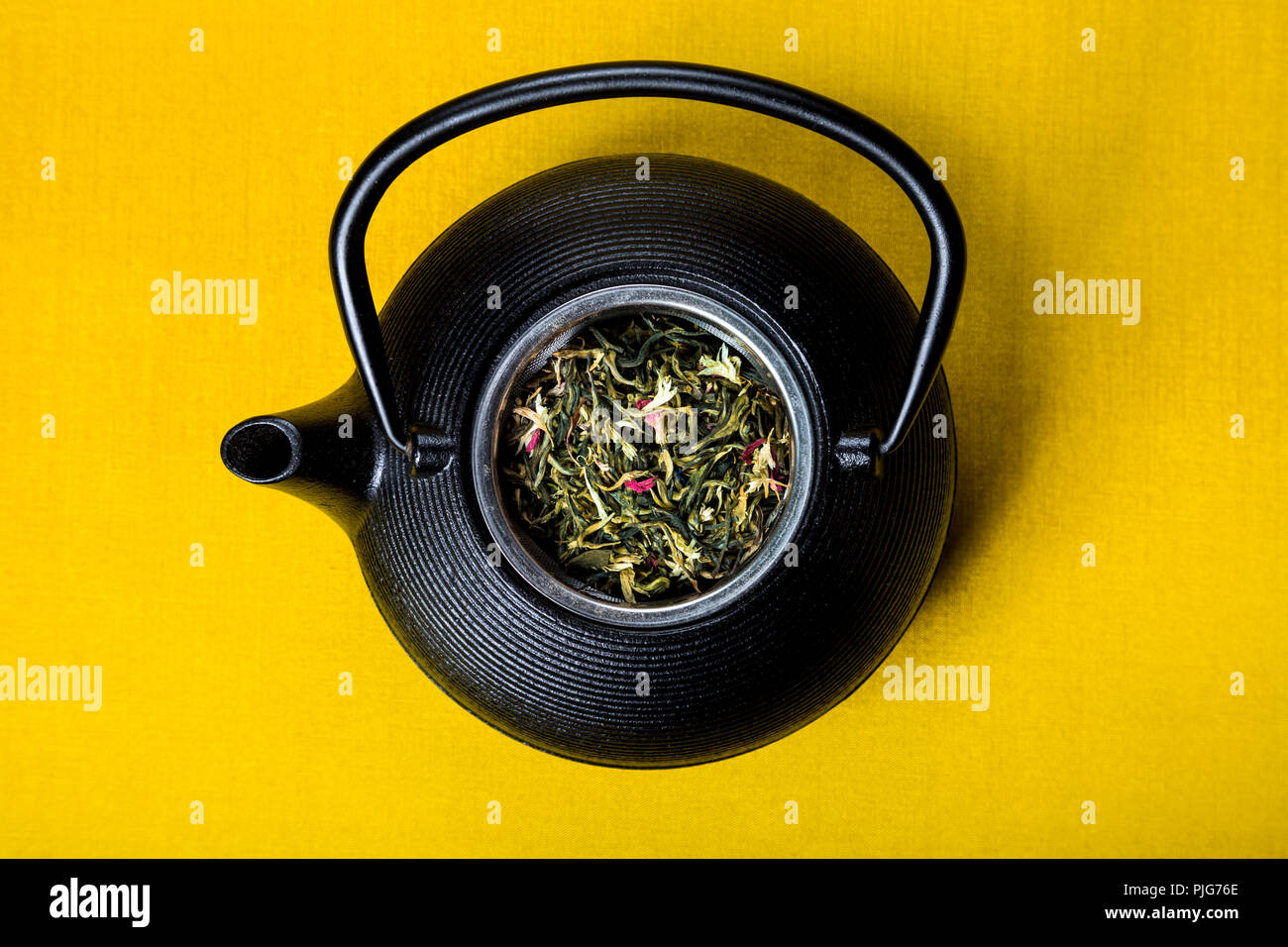 Cast Iron teapot (tetsubin) with loose leaf white tea against yellow background Stock Photo