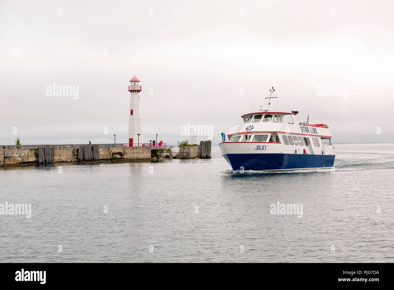 Tourists on a ferry approaching pier in St. Ignace Michigan. Wawatom lighthouse on the pier. Stock Photo