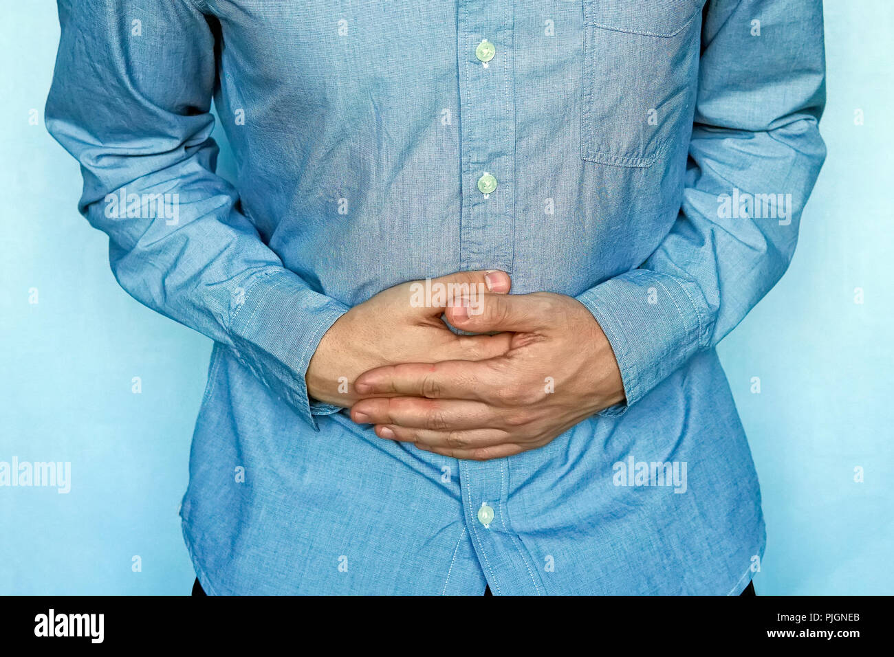 Young man with strong stomach pain on blue background. The young man clings to the stomach. Digestive problems. ulcerative bowel disease Stock Photo