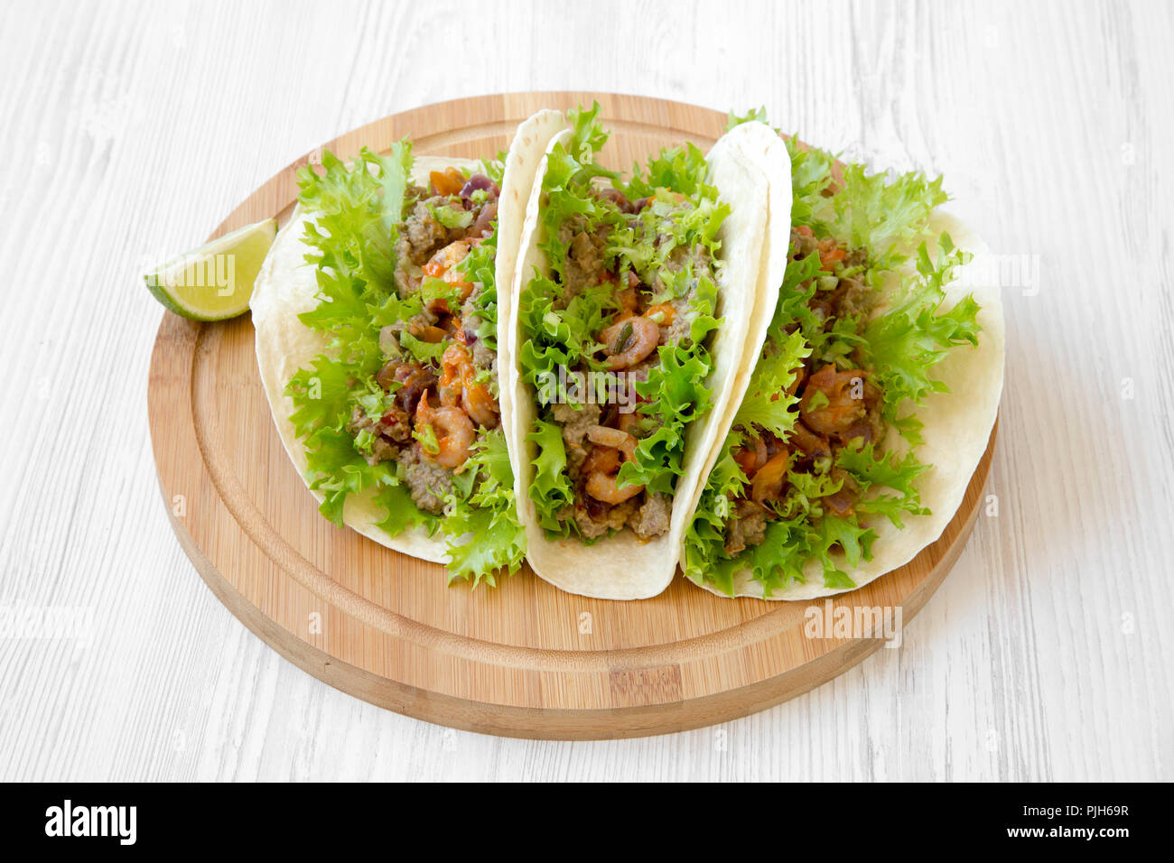 Shrimp tacos on round bamboo board on white wooden surface, low angle view. Mexican food. Stock Photo